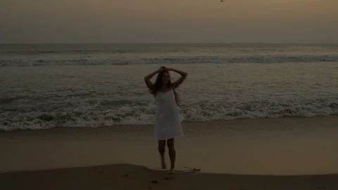 Young slim long haired young woman walks along the ocean. Pacific Ocean. Sunset. Stock Footage 155284110