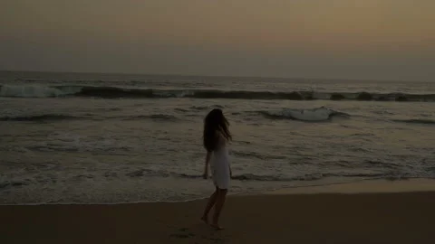 Young slim long haired young woman walks along the ocean. Pacific Ocean. Sunset. Stock Footage 155285295