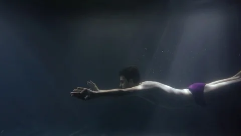 Young slim man dressed swimming trunks and red socks is swimming underwater in Видео 105033485