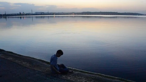 Young slim man throws stones on water in the evening Stock Footage 87795025