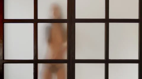 Young slim model moves slowly behind matt glass, white background, loop effect Stock Footage 274057013