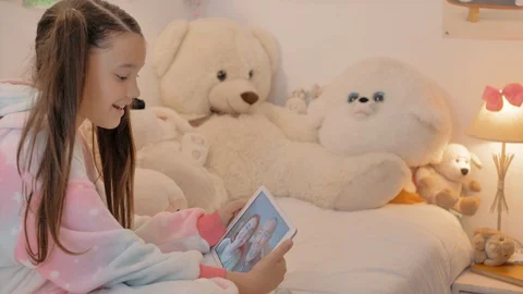 Young small girl in pajamas happily talks to parents on tablet together teddies Stock Footage 129059341