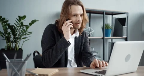 Young smart stylish office worker with long hair sitting at work talking on cell Stock Footage 147051262
