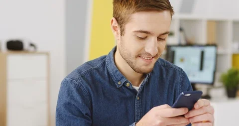 Young smiled attractive man chatting, taping and typing on the smartphone in the Stock Footage 88463637