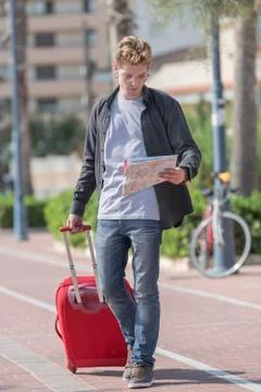 Young smiles looking at a map in a smiling way wearing a grey shirt and a blu Stock Photos