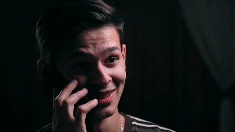Young smiley man talking on the phone in the dark room, close up Stock Footage 99050760