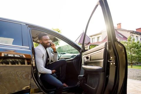 Young smiling african man using smartphone while sitting on passenger seat in 库存照片