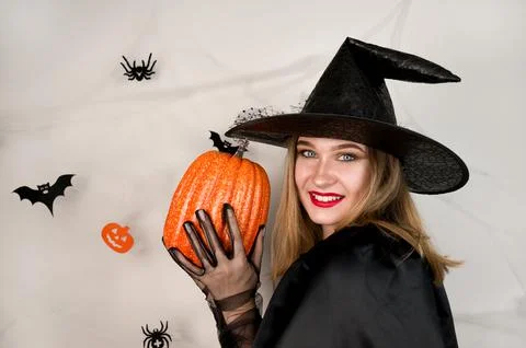 Young smiling blonde dressed as a witch holding pumpkin against halloween bac Stock Photos