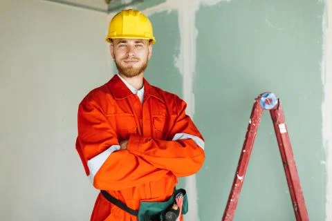 Young smiling builder in orange work clothes and hardhat happily Foto stock