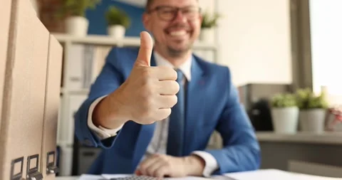 Young smiling businessman sitting at table and showing thumb up 4k movie Stock Footage 246911140