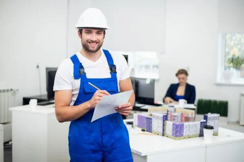 A young smiling construction worker taking notes while in office Stock Photos