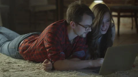 Young Smiling Couple are Laying on the Floor and Using Laptop at Home in Evening Stock Footage