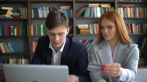 Young smiling couple sitting on couch and using laptop and credit card for Stock Footage 86184409