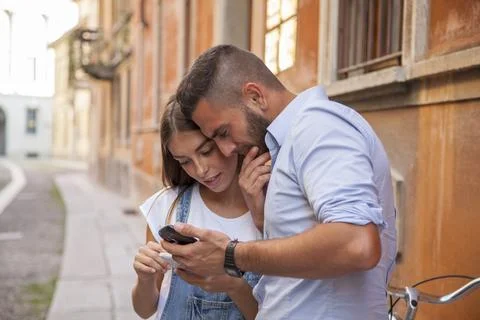 Young smiling couple using smartphone while riding bicycles through the str.. Stock Photos