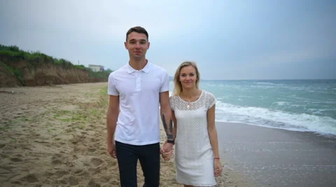 Young smiling couple walking along the beach and looking to camera slow motion Stock Footage 65204876