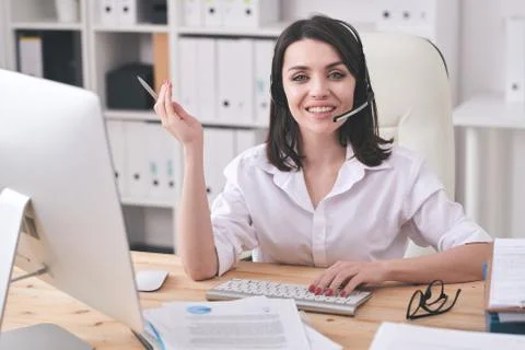 Young smiling customer support representative sitting by workplace 스톡 사진