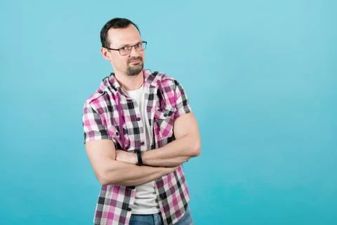 Young smiling guy with a beard in glasses and a klepy shirt folded his arms o Stock Photos