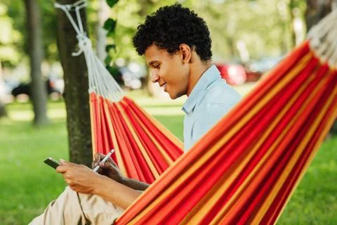 Young smiling guy drawing on digital tablet in park Fotos de archivo