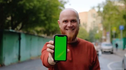 Young smiling guy holds out phone forward showing screen with green background 스톡 동영상 139001615