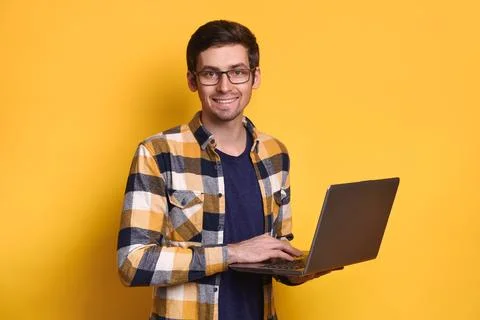 Young smiling guy posing with laptop against yellow studio wall Stock Photos