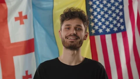 A young smiling guy stands against the background of the flags of Ukraine Stock Footage 237183005