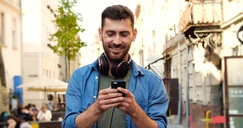 Young Smiling Handsome Guy using his Smartphone and Walking on Old town Center Stock Footage 99235349