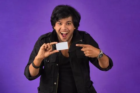 Young smiling handsome man posing with a credit card on purple background. Stock Photos