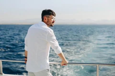 A young smiling happy man on the deck of a cruise ship looks towards the su.. Stock Photos