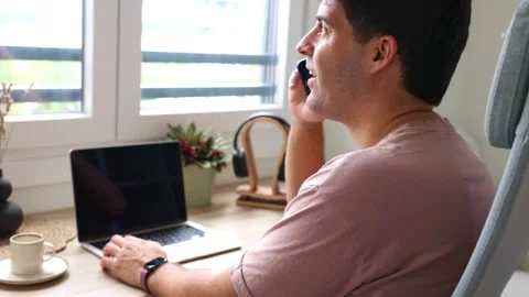 Young smiling hispanic man talking on a smartphone while teleworking from h.. Stock Footage 319027700