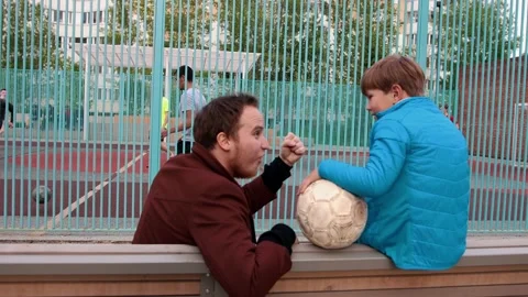 Young smiling man and his little brother sitting on the bench and watching other Stock Footage 132528907