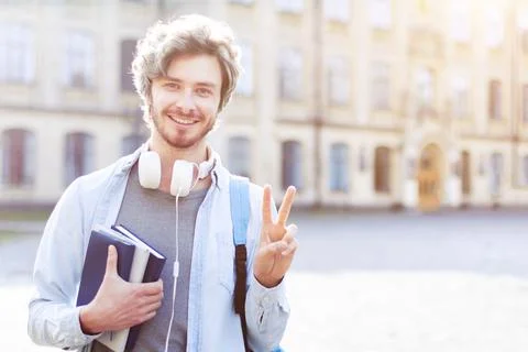 Young smiling man in backpack is holding books, standing outdoor on backgroun 스톡 사진
