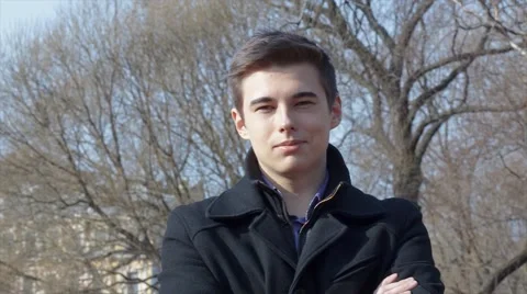Young smiling man in black coat looking at camera outdoor in park Stock Footage 61864981
