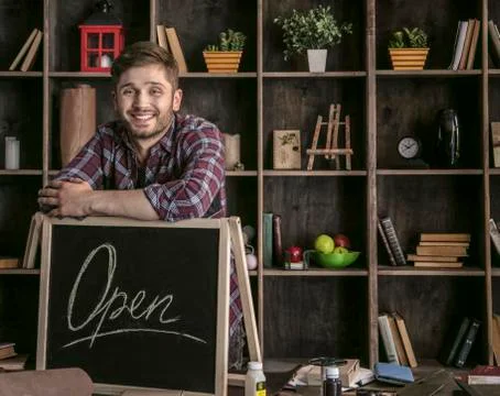Young smiling man leather worker standing near open sign at table with tools Stock Photos