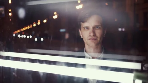 Young smiling man looking at camera standing alone on busy urban street at night Video stock 80009199