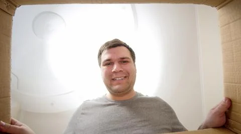 Young smiling man looking inside of parcel or gift box 写真素材