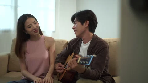 Young smiling man playing guitar together with happy beautiful woman while sitti Stock Footage 283830992