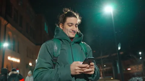 Young smiling man writing a message while standing outdoors under a street lamp Stock Footage 231690773