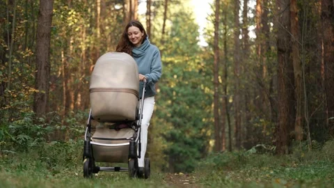 Young smiling mother walking with her baby boy in a stroller through a sunlit Video stock 346534715