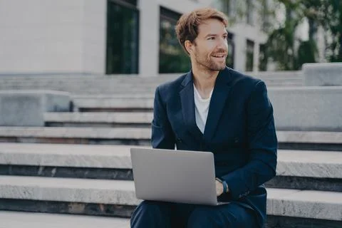 Young smiling office worker sitting outside on stairs in city center holding Stock Photos