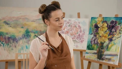 Young smiling painter holding a paintbrush in her hand and looking at Stock Footage 74205337