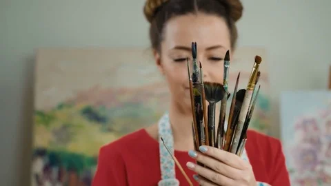 Young smiling painter holding paintbrushes in her hands and posing on camera Stock Footage 74196868