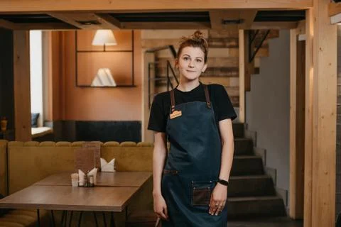 A young smiling waitress is posing in a restaurant. Stock Photos