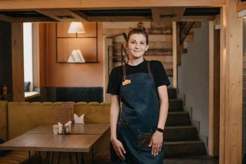 A young smiling waitress is posing in a restaurant. Stock Photos
