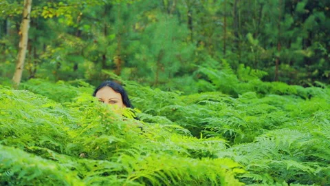 A young smiling witch in black clothes rises from a thicket of ferns and Stock Footage 94925408