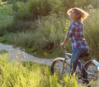 Young smiling woman on a bicycle in the park on sunset background Stock Photos