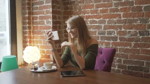 Young smiling woman having video conversation using smartphone in coffee shop Stock Footage 72017550