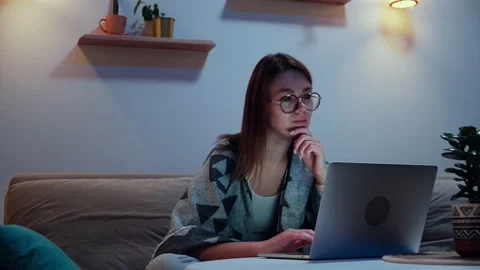 Young smiling woman using laptop at night, working overtime at home sitting on Stock Footage 220887350