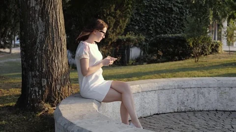 Young Smiling Woman Using Smartphone Sitting on Bench In Park At The Sunset Stock Footage 79877339