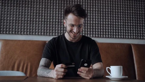 Young smily guy in a glasses, shops online through his smart phone. Holding Stock Footage 106093430
