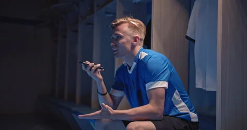 Young soccer player, man talking with phone sitting in the locker room at the Stock Footage 139205288